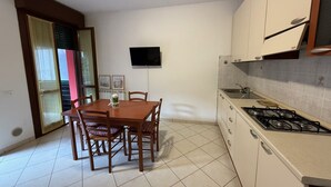 Una cucina compatta con tavolo e sedie, TV a muro e piano cottura a gas.
