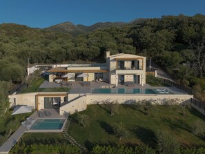 A modern two-story house with a swimming pool, outdoor seating, and a view of the surrounding forest. - Azura Exclusive Villa (Acharavi)