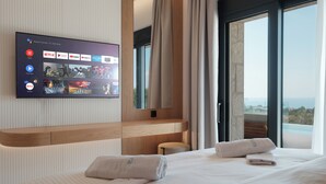 Ein Hotelzimmer mit einem großen Flachbildfernseher, der Streaming-Dienste anzeigt, einem Holz-Kopfteil, einem Bett mit ordentlich gefalteten Handtüchern und einem Balkon mit Blick.