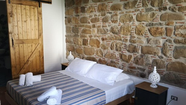 A bedroom with a stone wall, a wooden bed, two bedside tables, and a wooden door. - Anemone is an independent apartment consisting of an equipped kitchen-living room with a single sofa bed, a double bedroom overlooking the main square and the sea, and a bathroom made of handmade ceramic, equipped with a washing machine. The accommodatio (SANTO STEFANO DI CAMASTRA - ME)