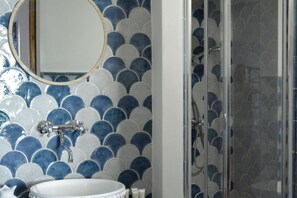 A bathroom with a sink, mirror, and shower. - Anemone is an independent apartment consisting of an equipped kitchen-living room with a single sofa bed, a double bedroom overlooking the main square and the sea, and a bathroom made of handmade ceramic, equipped with a washing machine. The accommodatio (SANTO STEFANO DI CAMASTRA - ME)