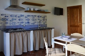 A compact kitchen with a gas stove, a sink, and a tiled backsplash featuring fish patterns. There is a wooden shelf above the stove and a television mounted on the wall. - Anemone is an independent apartment consisting of an equipped kitchen-living room with a single sofa bed, a double bedroom overlooking the main square and the sea, and a bathroom made of handmade ceramic, equipped with a washing machine. The accommodatio (SANTO STEFANO DI CAMASTRA - ME)