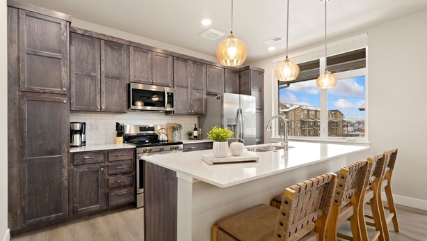 A modern kitchen with dark wood cabinets, stainless steel appliances, a large island with bar stools, and pendant lighting. - The Landmark 2 King Beds, Garage & Fireplace (Fort Collins)