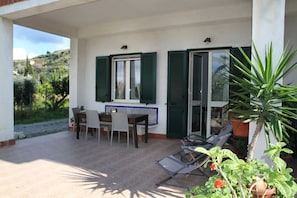 Portico coperto con tavolo e sedie, un piccolo tavolino con una pianta e una poltrona con cuscino.