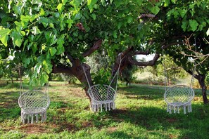 Three white wicker chairs hanging from a tree in a grassy area. - Located just a few meters from the sea and surrounded by a large Mediterranean garden, Tenuta Piana is the ideal place for those seeking relaxation, nature, and authenticity. The property offers direct access to a private beach and a peaceful environment (Marina di Caronia)