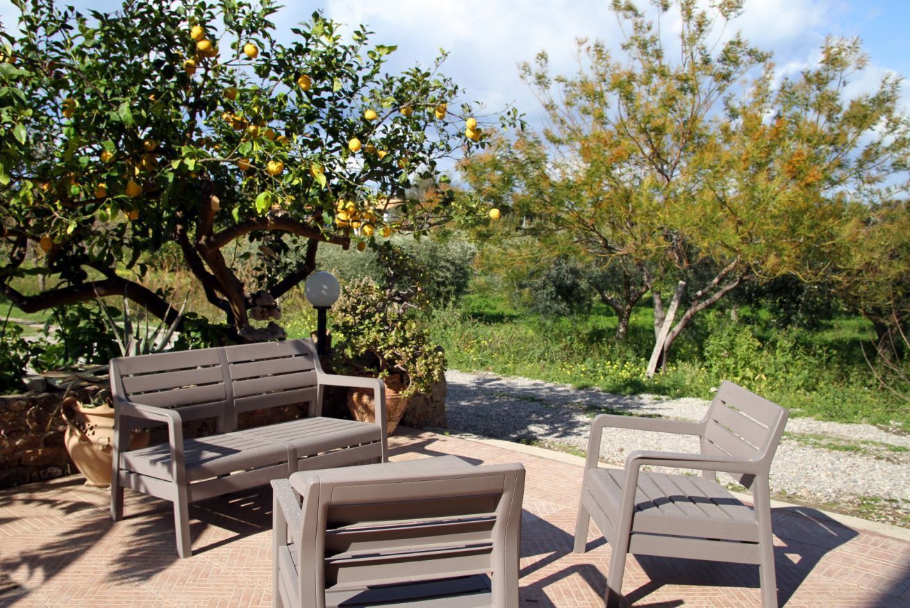 Un espace extérieur aménagé avec un banc et une table, entouré d’arbres et de plantes.