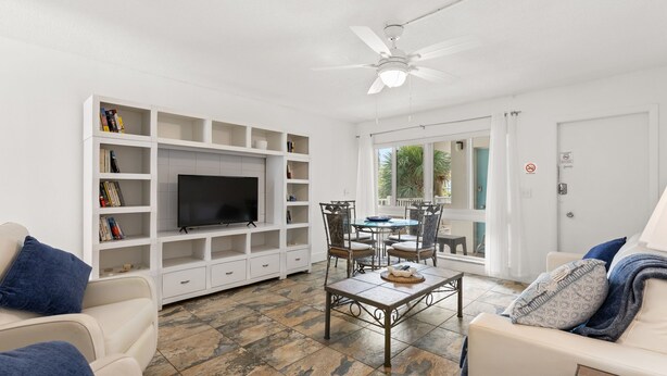 A living room with a TV, white shelves, a dining table with chairs, and a ceiling fan. - Pompano 3225 20A (Pompano Beach)