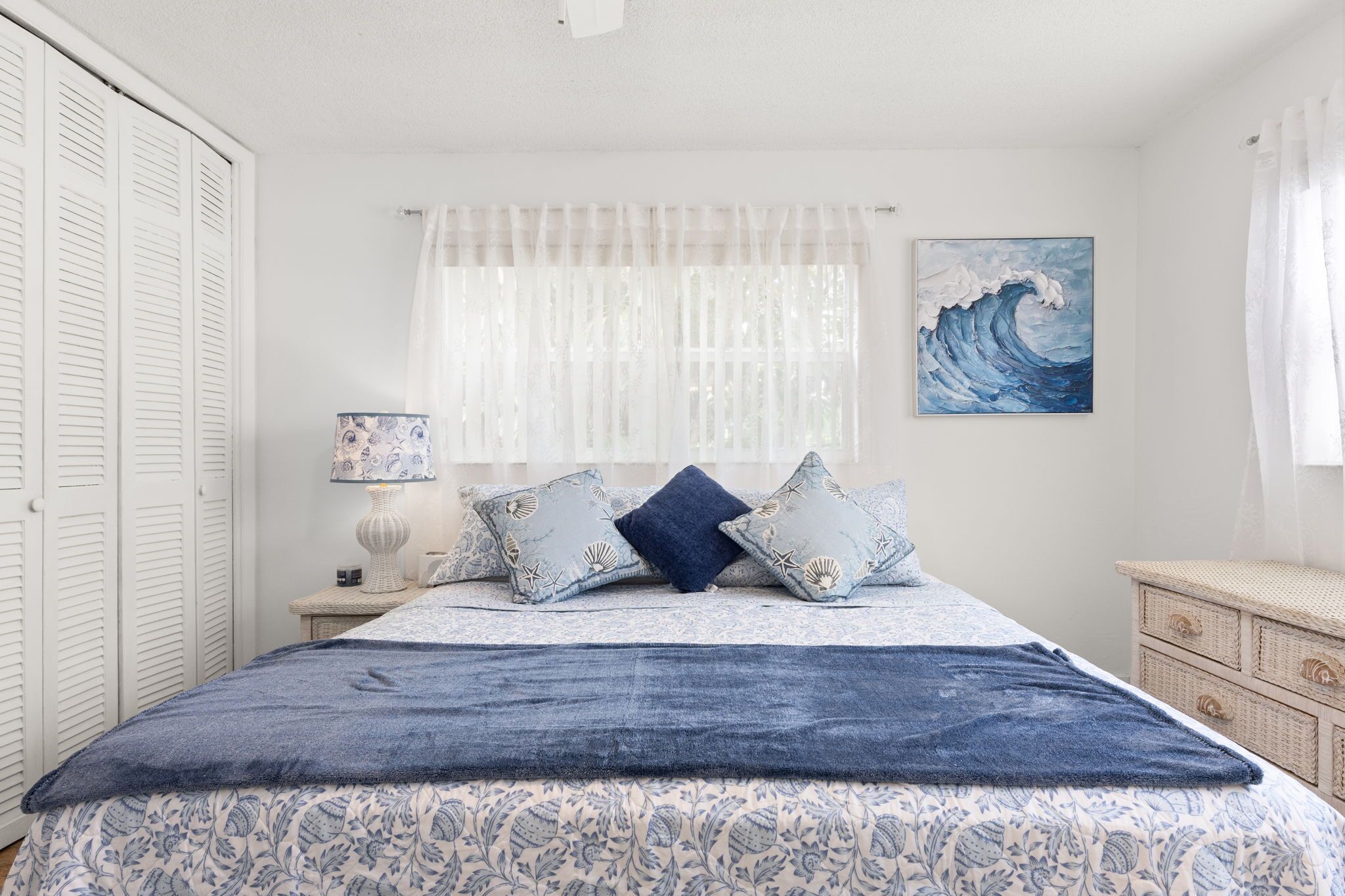 A bedroom with a bed, a nightstand, a lamp, a painting, and a window with curtains.