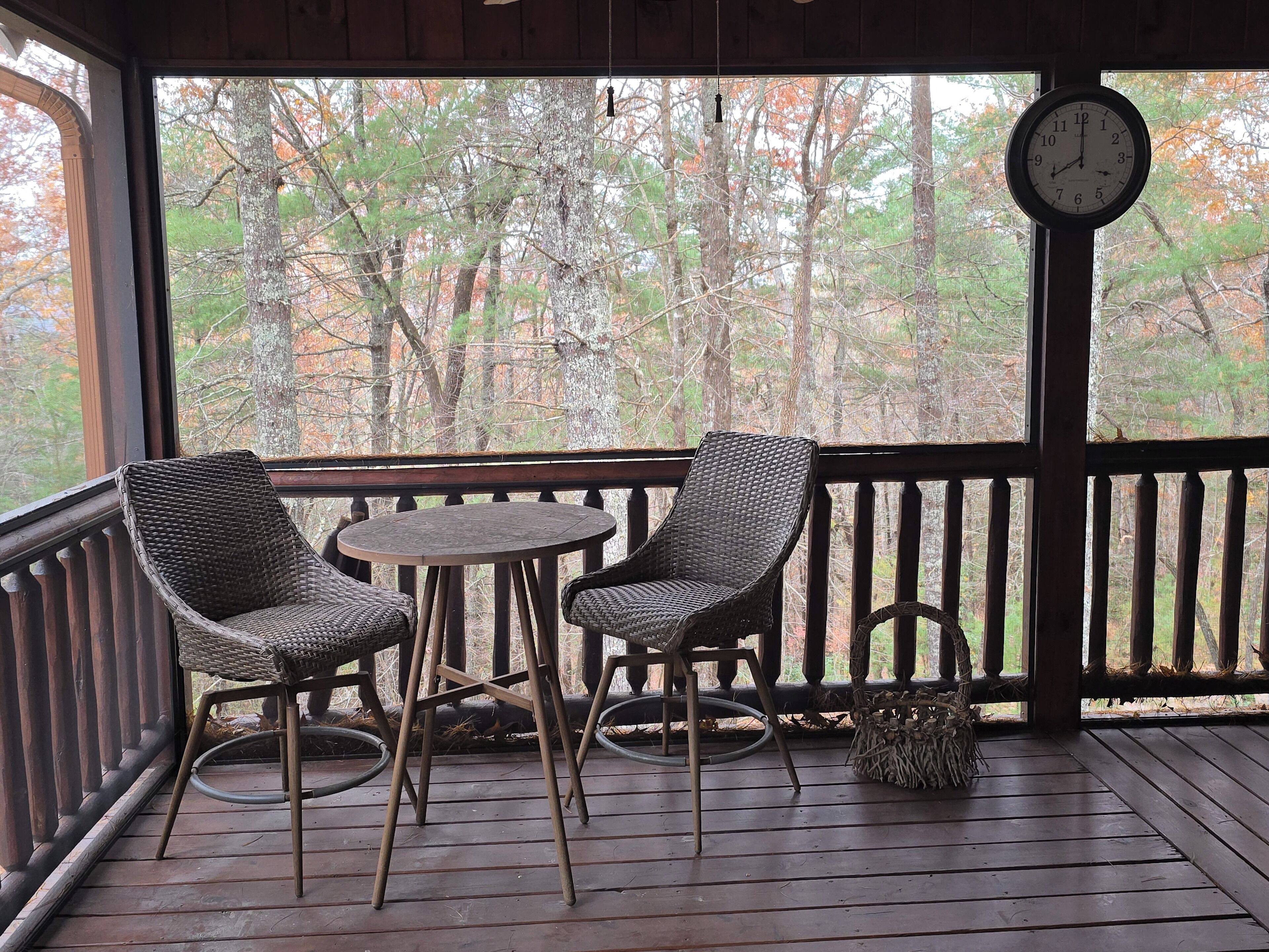 A wooden deck with wicker chairs and a small round table, overlooking a forested area.