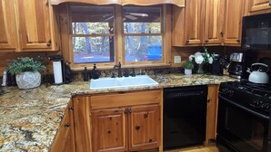 A kitchen with wooden cabinets, a granite countertop, a dishwasher, a stove, and a window with a view of the outdoors. - Blue Ridge, North GA Cabin: Sleeps 10 & 2 pets • hot tub • Fast wifi • fire pit (Blue Ridge)
