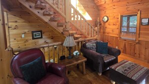 A wooden cabin interior with a staircase, leather armchair, sofa, ottoman, and a small table with a lamp. - Blue Ridge, North GA Cabin: Sleeps 10 & 2 pets • hot tub • Fast wifi • fire pit (Blue Ridge)
