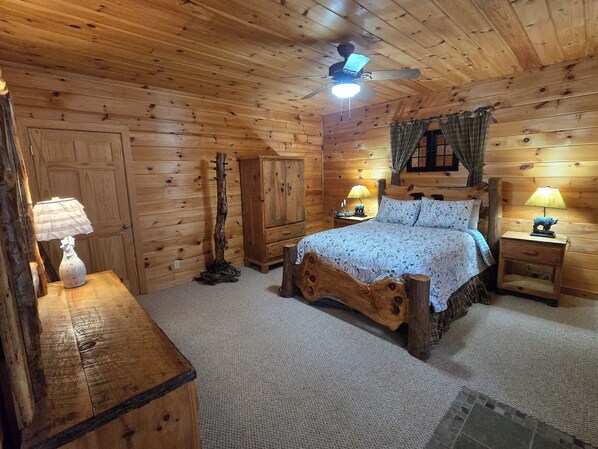 A cozy log cabin bedroom with a wooden bed, two bedside lamps, a nightstand, a wardrobe, and a ceiling fan. - Blue Ridge, North GA Cabin: Sleeps 8, hot tub, Fast Starlink wifi • fire pit (Blue Ridge)