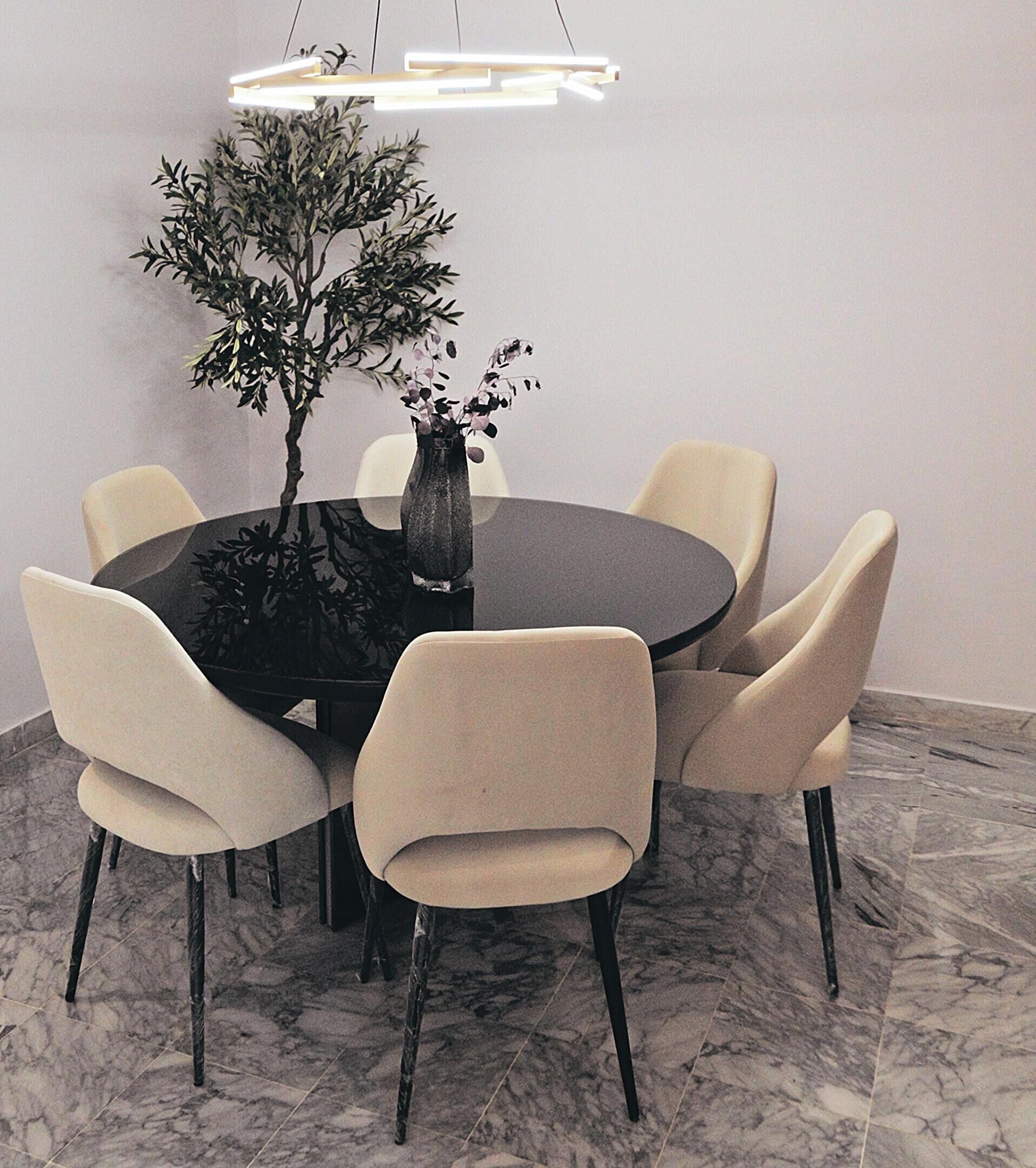 Une table de salle à manger ronde, accompagnée de six chaises, un vase rempli de fleurs et un luminaire suspendu au design moderne.