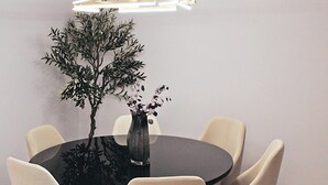A round dining table with six chairs, a vase with flowers, and a modern pendant light.