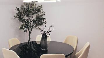 Une table de salle à manger ronde, accompagnée de six chaises, un vase rempli de fleurs et un luminaire suspendu au design moderne.