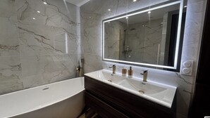 Ein modernes Badezimmer mit einer freistehenden Badewanne, einem Waschtisch mit großem Spiegel und Marmorwänden.