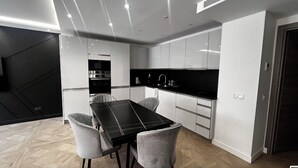 Eine moderne Küche mit schwarzer Arbeitsplatte, weißen Schränken und einem Essbereich mit einem schwarzen Tisch und zwei Stühlen.