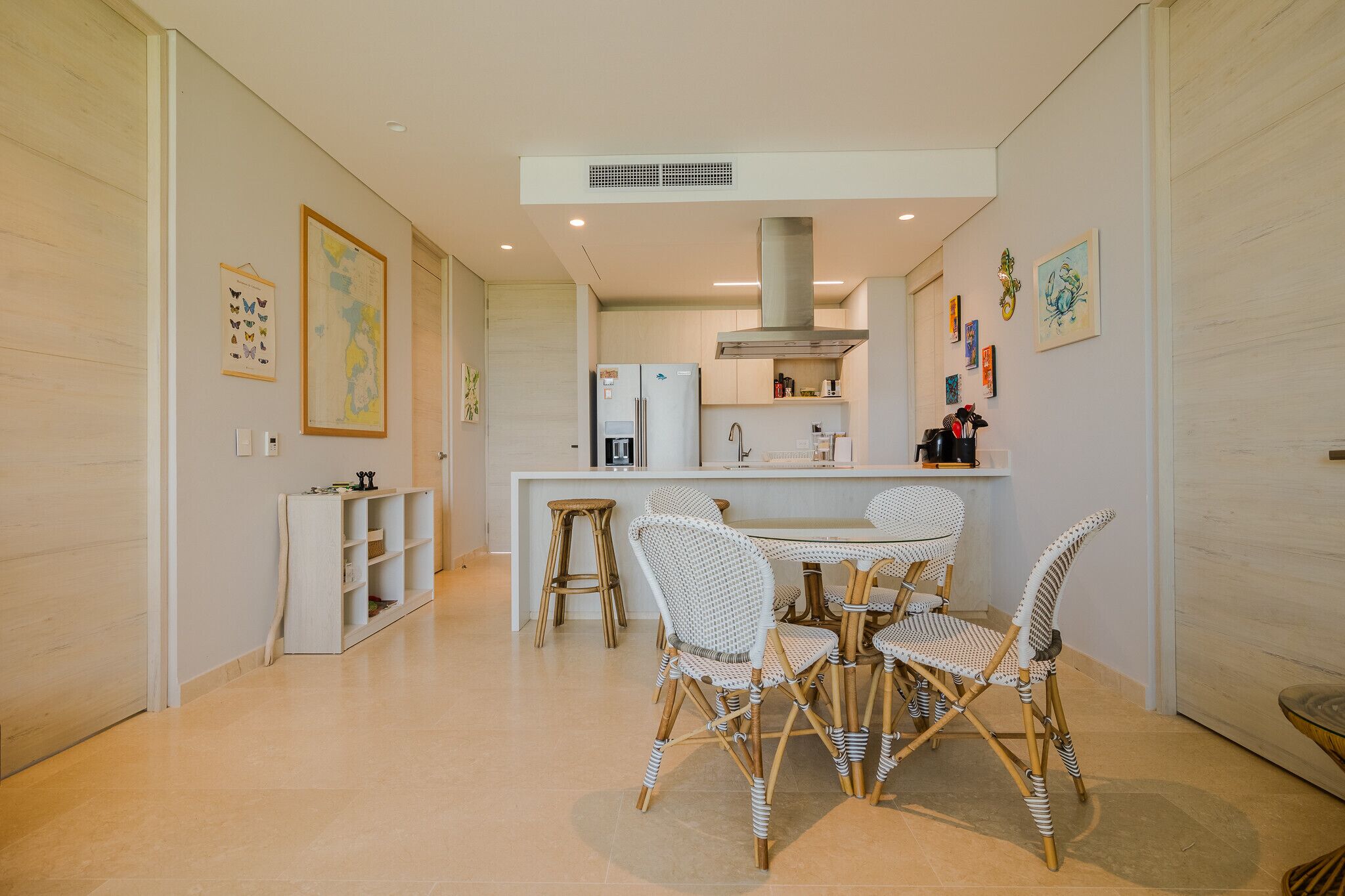 A modern kitchen with white cabinetry, a central island with stools, and a dining area with wicker chairs.