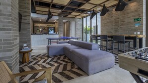 Un espace de détente moderne comprenant un canapé, une table de baby-foot et un bar avec un comptoir et des sièges.