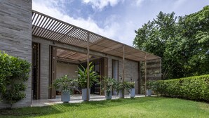 Une maison moderne dotée d’un patio couvert, de grandes fenêtres et de plantes en pot.