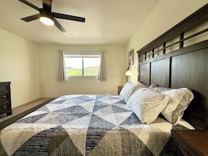 A bedroom with a large bed, a ceiling fan, a window with curtains, and a nightstand with a lamp. - Modern Resort Home @ Starr Pass Golf Resort (Tucson)