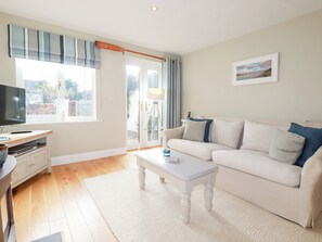 Ein Wohnzimmer mit einer Couch, einem Couchtisch, einem Fernseher und einem Fenster mit Vorhängen.