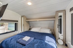 Een slaapkamer met een bed, kussens, een televisie en een raam.