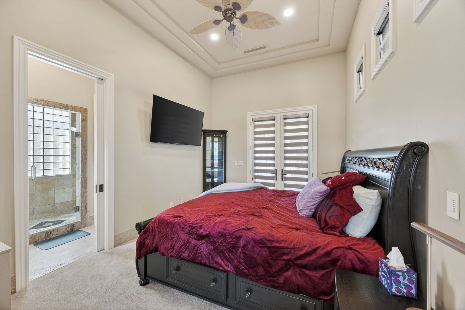 A bedroom with a bed, a TV, a ceiling fan, and a door leading to a balcony.