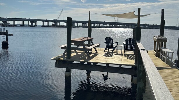A wooden dock extending into calm water with a picnic table and chairs, a canopy, and a distant bridge. - Manatee Riverfront Home , Cozy 2-bedroom house in Ellenton “Duplex”, left side.  (Ellenton)