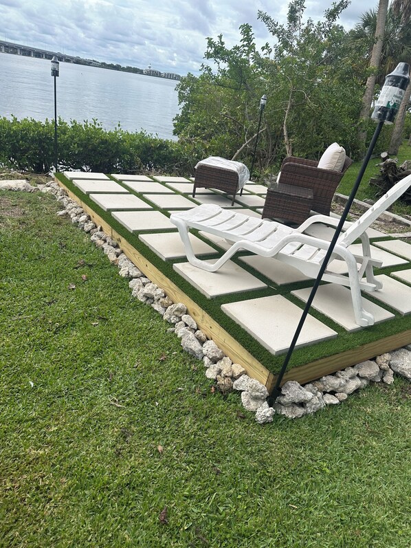 A poolside area with a seating arrangement, a view of the water, and a bridge in the background.