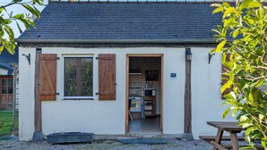 A small building with a dark tiled roof, wooden shutters, and a visible kitchen area with a stove and sink.