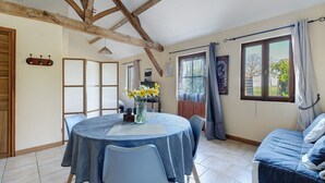 A dining area with a round table, chairs, and a vase of flowers. There is a bed with a blue cover in the room.