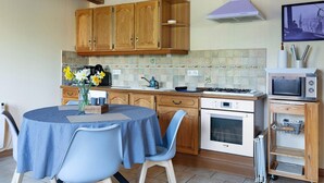 A kitchen with wooden cabinets, a stove, an oven, a microwave, a dining table with chairs, and a vase with flowers.
