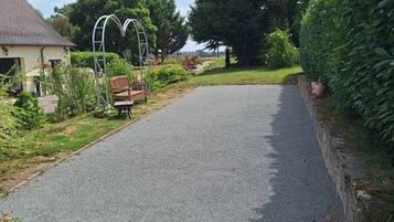 A paved driveway leading to a house with a garden, a wooden bench, and a metal archway.