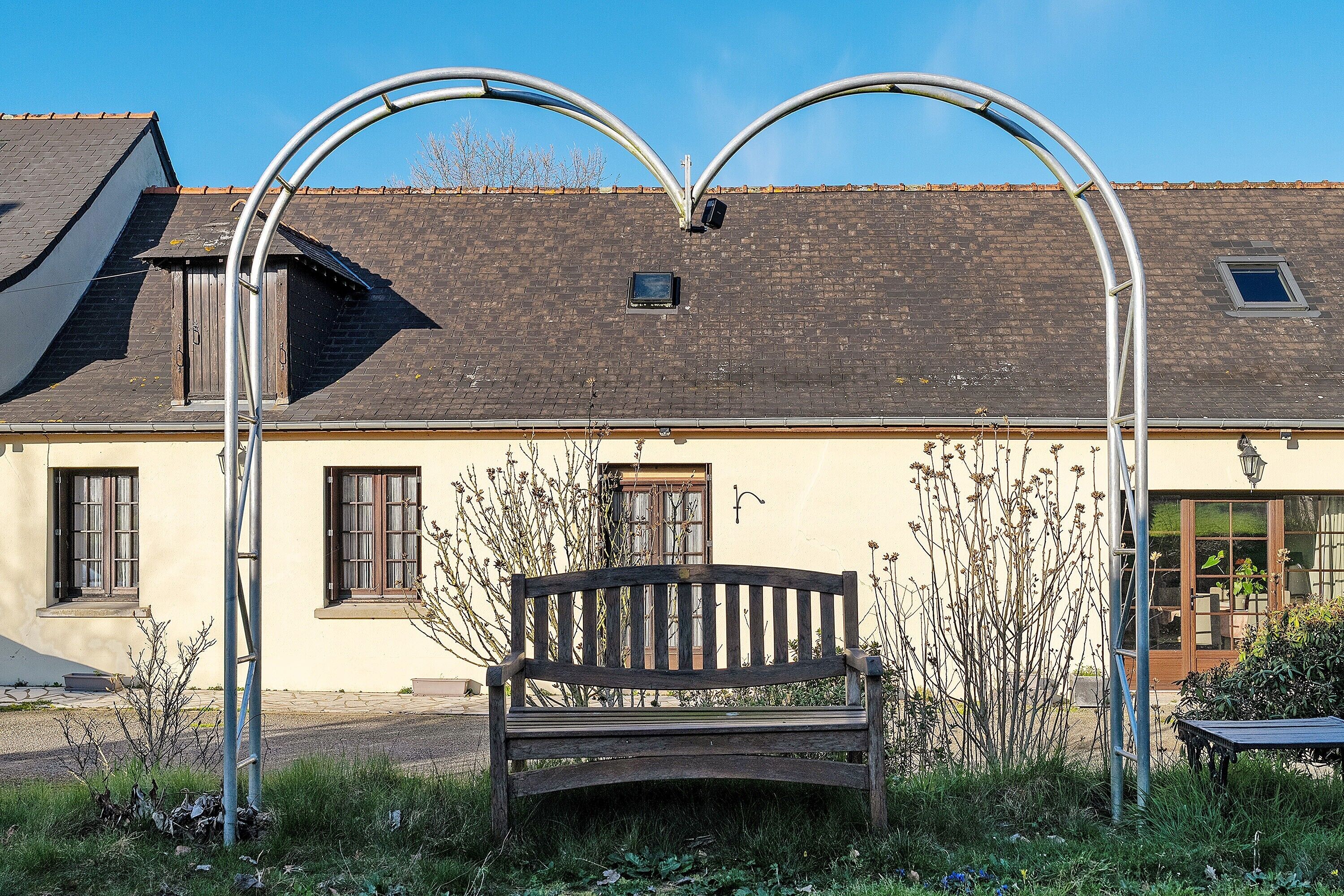 A bench in front of a building with a sloped roof and two windows.