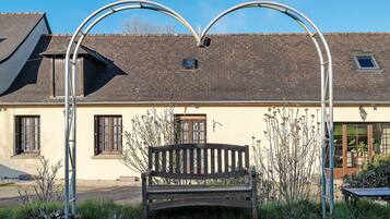 A bench in front of a building with a sloped roof and two windows.