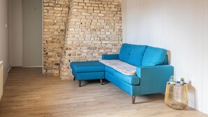 Una habitación con un sofá seccional azul, piso de madera, pared de ladrillo y pared blanca con paneles.