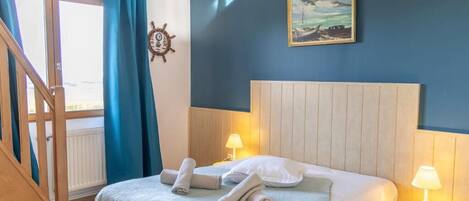 Een slaapkamer met een bed, twee bedlampen, een scheepsschroef en een schilderij aan de muur.