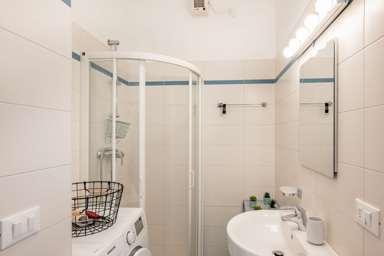 A modern bathroom with a glass-enclosed shower, a sink with a mirror, and a washing machine.