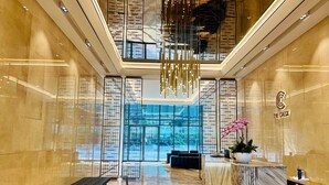 A modern hotel lobby with a marble reception desk, a large glass window, and a decorative chandelier. - Metropole The Crest Thu Thiem Apartment (Ho Chi Minh City)