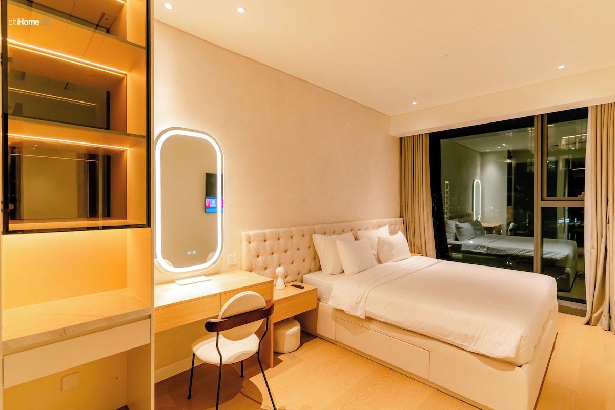 A hotel room with a bed, a desk with a chair, a mirror, and a large window.