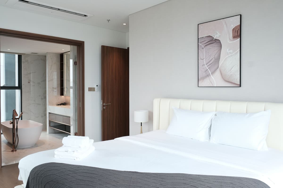 A modern hotel room with a large bed, a bathroom with a freestanding bathtub, and a wall-mounted artwork.