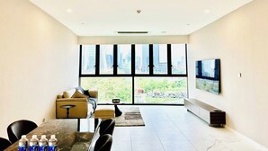 A modern hotel room with a large window offering a city view, a dining area with a marble table, and a seating area with a sofa and a coffee table. - Metropole The Crest Thu Thiem Apartment (Ho Chi Minh City)