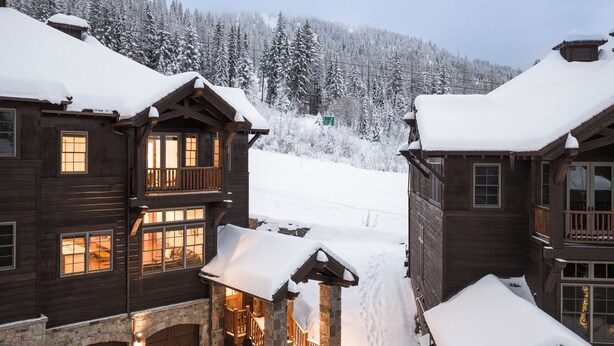 A wooden cabin with a stone archway entrance, a balcony, and a snow-covered roof. - Luxury at Whitefish Mountain chalet w/ hot tub (Whitefish)