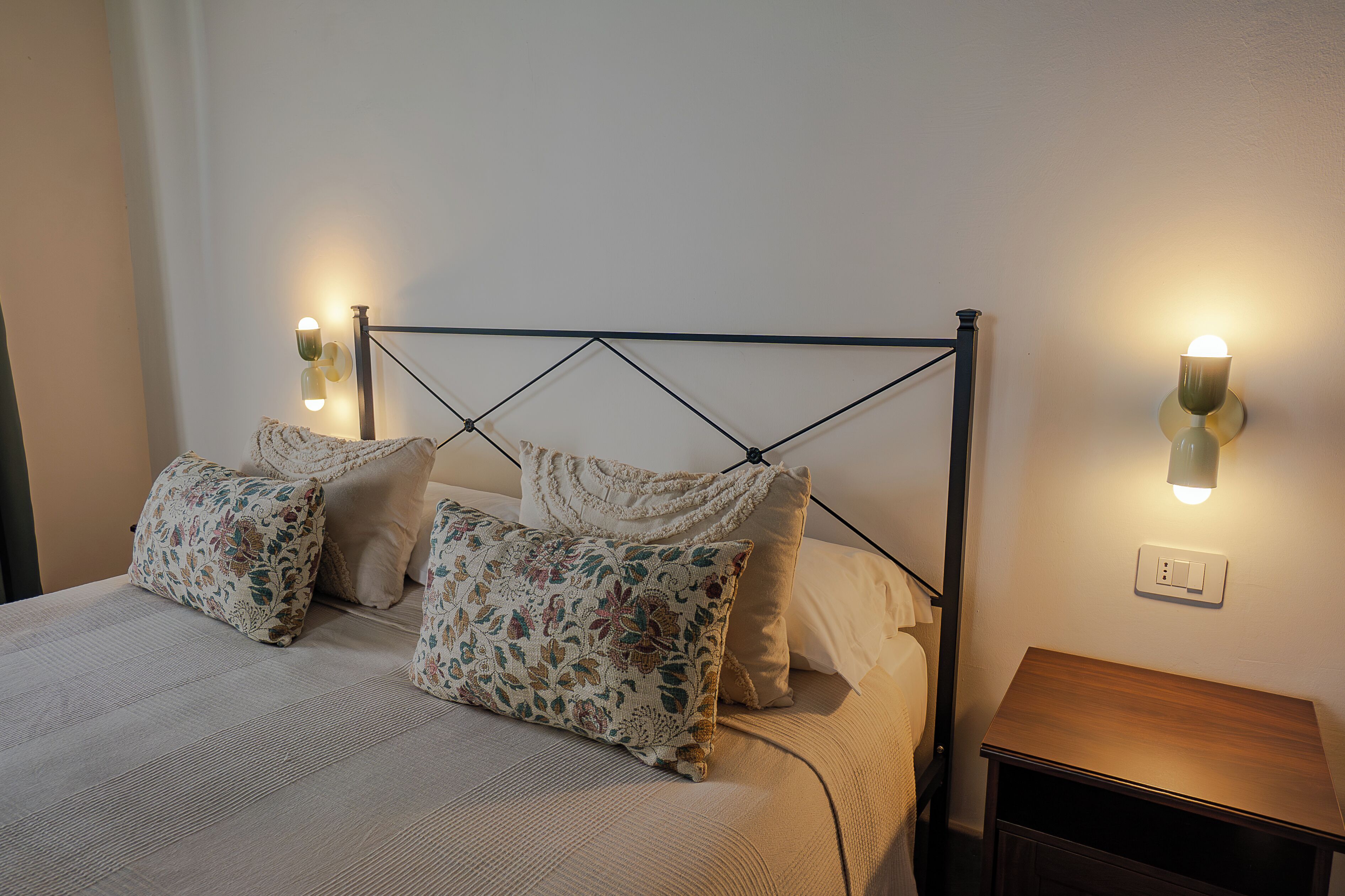 A neatly made bed with floral-patterned pillows, a headboard with a geometric design, and bedside lamps.