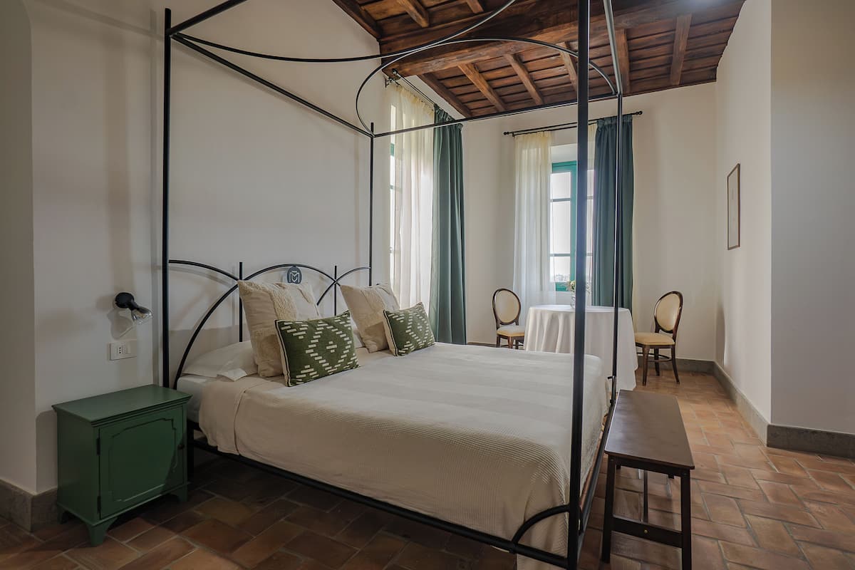 A bedroom with a four-poster bed, a green nightstand, a wooden bench, and a small table.