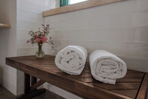 Una mesa de madera con dos toallas blancas enrolladas y un jarrón con flores rosadas.
