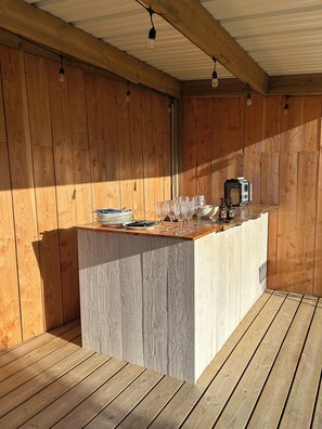 Een houten terras met een barhoek, inclusief een aanrecht, glazen en een broodrooster.
