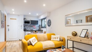 A modern living room with a yellow sofa, a coffee table, and a dining area with a kitchen in the background.