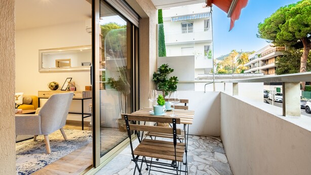 A balcony with a table and chairs, a potted plant, and a view of buildings and trees.